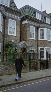 Woman strolling past charming brick houses in chelsea london uk on a quiet street corner with lush greenery and traditional architecture.