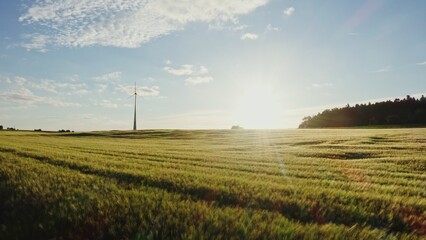 The light of the rising sun illuminates the picturesque green meadow on which the wind generator...