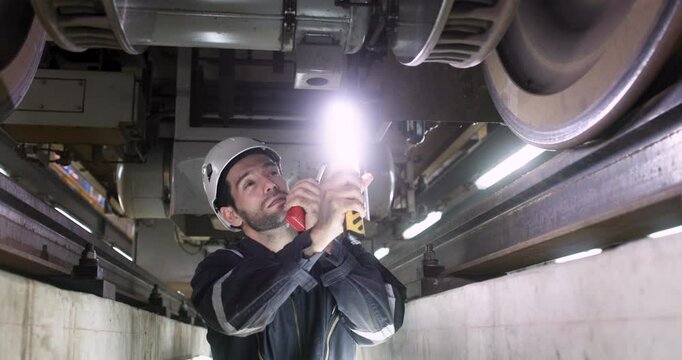 The engineer is depicted meticulously inspecting the train's equipment and machinery underbody suspension of the electric train in a railway garage.