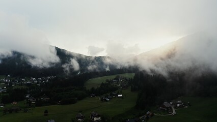 Dramatic drone view of a mountain valley with a village in a lowland with low hanging clouds covering the mountain tops. Austria, Alps video filming at dusk