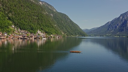 The boat floats on a picturesque mountain lake near the village of Hallstatt, located on a mountainside. Austria, Alps, drone video on a sunny day