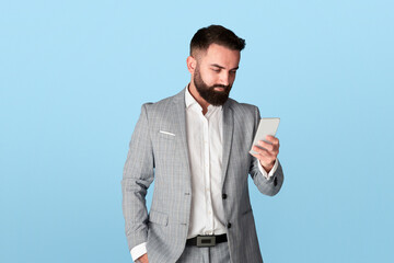 Millennial office employee communicating on smartphone against blue background