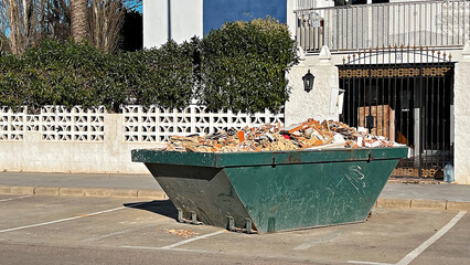 Green skip bin filled with construction rubble and debris near residential building