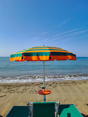 Orange and green beach umbrellas. Blue sky. Relaxing context. Summer holidays at the sea. General contest and location