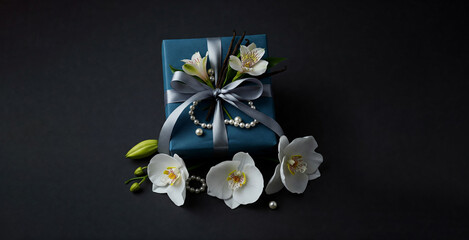 White flowers on black background and gift box wrapped in a blue paper