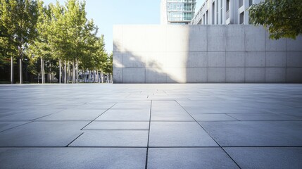 Obraz premium An empty stone tiled plaza reveals a soothing environment, embraced by concrete walls and trees, capturing the tranquility of a bright day. The minimalistic layout invites reflection