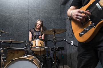 Fototapeta premium Female drummer playing drum kit in professional soundproof rehearsal studio. Rock band practice session with live music performance and rhythmic drumming.