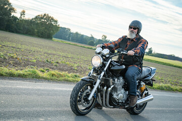 Motorr&auml;der - kultiger Biker f&auml;hrt auf seinem Motorrad eine Landstrasse entlang, labelfrei und retuschiert.