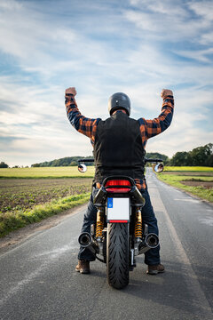 Motorradfahrer auf seiner Maschine von hinten in Siegerpose, R&uuml;ckansicht.