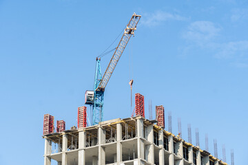 A crane operates at a construction site, lifting materials for a high-rise building. Workers are busy on the structure under a clear blue sky © Роман Булатов