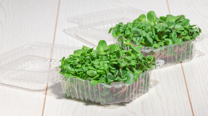 Freshly harvested microgreens in plastic containers on a white wooden table, ideal for health-conscious meals.