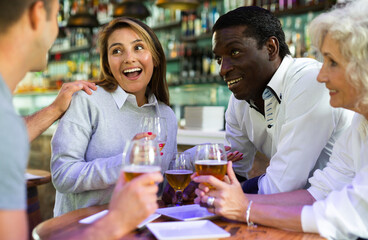 Cheerful international friends different ages enjoying pinchos and beer in the evening pub