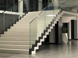 Modern staircase with a minimalist design, featuring glass railings, geometric shapes, and a sleek black-and-white contrast. The space is well-lit and decorated with contemporary elements like a geome