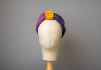 Crochet head band with a grey background on a head display stand 