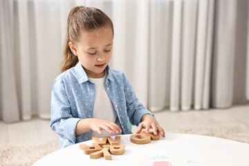Little girl learning alphabet with wooden letters at white table indoors, space for text