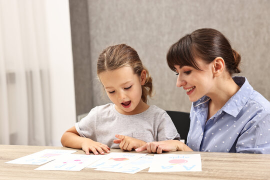 Smiling speech therapist working with little girl at table in autism treatment center