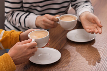 Coffee break. Women with cups of hot drinks at wooden table indoors, closeup