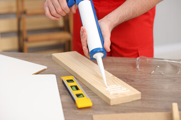 Worker with caulking gun glueing wooden plank indoors, closeup
