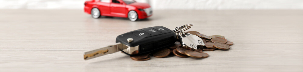 Car key, model and coins on light wooden table, selective focus. Buying auto