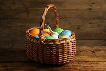 Beautiful decorated Easter eggs and bunny figure in wicker basket on wooden table