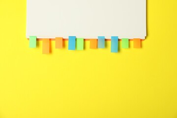 Notebook with colorful tabs on yellow background, top view. Space for text