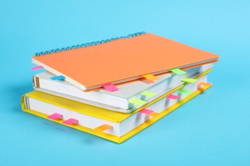 Books and notebook with colorful tabs on light blue background, closeup