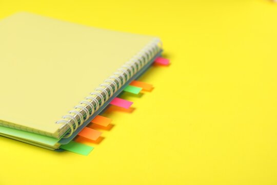 Notebook with colorful tabs on yellow background, closeup. Space for text
