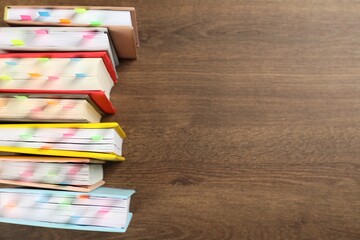 Books with colorful tabs on wooden table, top view. Space for text