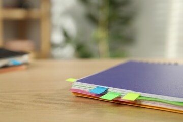 Notebook with colorful tabs on wooden table indoors, closeup. Space for text