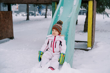 Little girl sliding down a snow-covered colorful slide