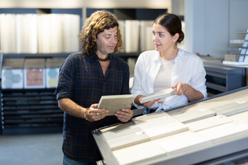 Obraz premium In construction mall,wife with husband inspects drawing of decorative slabs for interior decoration. Turnkey repairs, finishing materials, apartment renovation