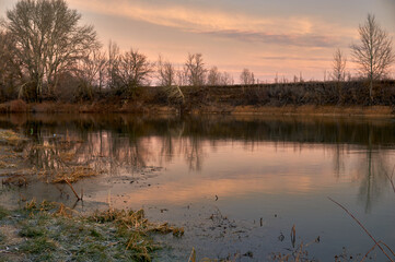 Dawn on the river, the sun has almost peeked over the horizon, its light is reflected on the surface of the river, the winter is warm and there is no snow, and the river is not covered with ice