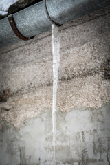 Long Icicle Hanging from a Metal Gutter in Winter.
