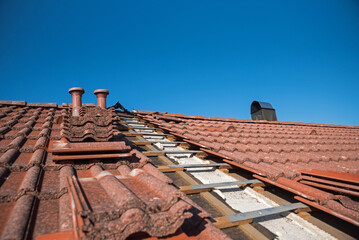 Partially uncovered house roof to replace the old roof tiles. two ventilation chimneys above