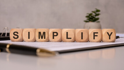 Wooden cubes spelling SIMPLIFY on office documents, symbolizing efficiency, clarity, and minimalism