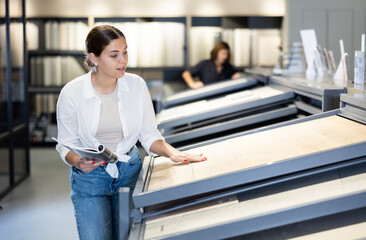 wistful customer stands at showcase with samples of parquet boards. customer compares color of...