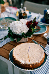 Cake with a cut out sector and a candle stands on a plate near a bouquet of flowers on the table