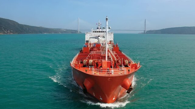 Large red oil tanker ship navigating through Bosphorus, creating a bow wave as it moves forward, with various deck equipment including anchor winches and a mast. Maritime navigation challenges
