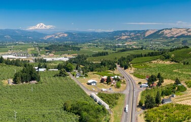 Aerial view of a rural orchard and highway intersection. Farm buildings and a highway are visible. A semi-truck travels along the road.  Odell, Oregon, United States © Zenstratus