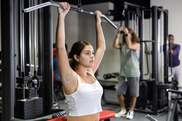Fototapeta premium Caucasian woman training on lat pull down machine in gym
