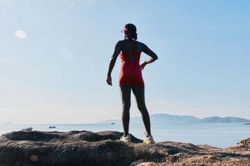 Woman standing on rocks by the sea during daytime, wearing a red swimsuit, embracing a moment of tranquility
