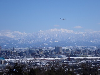 2025年2月25日雪景色の富山市街地と冠雪の北アルプ氏と旅客機