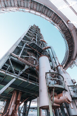 Low-angle view of an industrial metal structure with pipes, platforms, and rusted details against a...