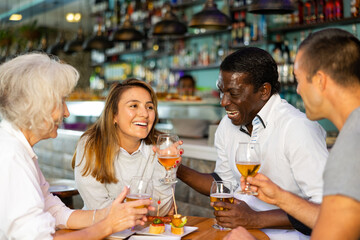 Company of multiracial friends drinking beer and talking with each other during the rest in a pub