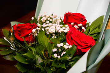 A bouquet of three roses in light green decorative paper with a red bow as an ideal gift for a loved one