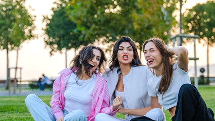 Fototapeta na wymiar Three young female friends chatting and having fun together in a grassy park on a summer day.
