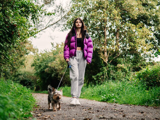 Young teenager girl with her small cute Yorkshire terrier on a walk in a forest park. Taking care of your pet theme. Model has slim body type and long rich hair. Selective focus.