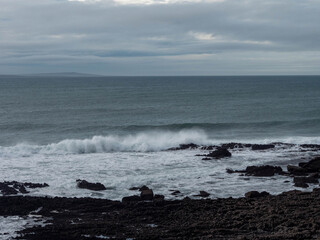 Rough stone coast, ocean waves and Aran islands in the background. Cloudy sky, Burren area, Ireland. Irish nature scenery. Nobody.