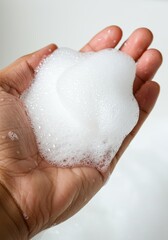 Fototapeta premium Close-up of a hand holding a generous amount of fluffy white foam, possibly soap or cleanser.