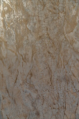 Textured wall with a cracked, marbled pattern in shades of gold and gray, resembling aged plaster.